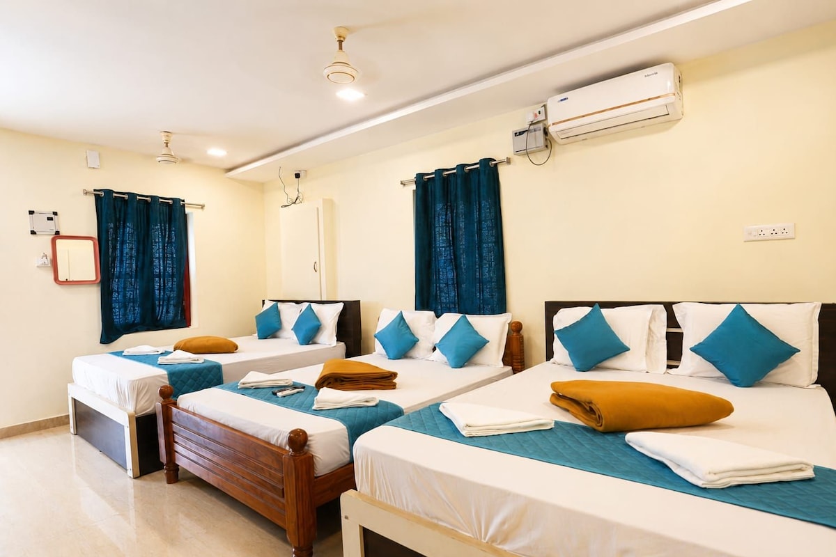 Habitación de hotel con cuatro camas, aire acondicionado, ventilador de techo y un espejo en la pared.