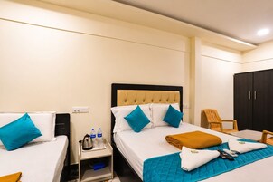 Una habitación de hotel con dos camas, un armario, una mesita de noche con hervidor y una silla.