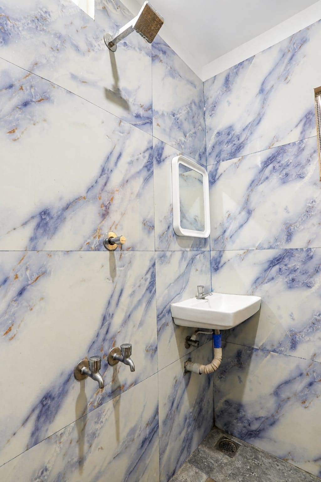 A bathroom with a marble wall, a sink, a mirror, and a shower.