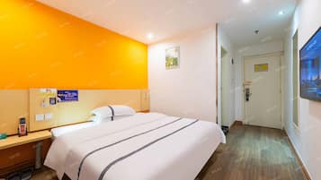 Una habitación de hotel con cama, mesita de noche y televisor montado en la pared.