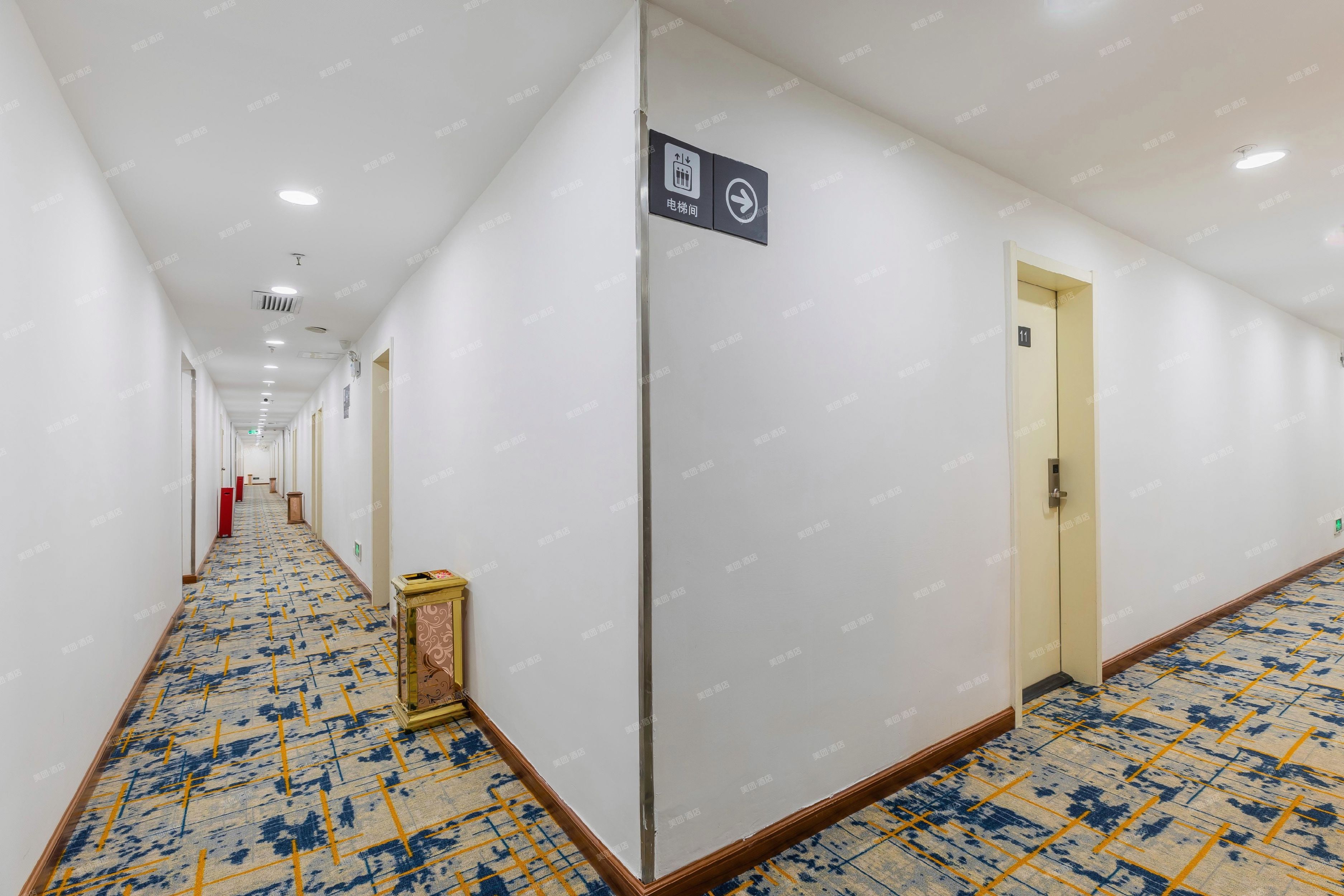 Een hotelgang met een kamerbreed tapijt, een bordje dat een liftzone aangeeft, en een deur met het nummer 11.
