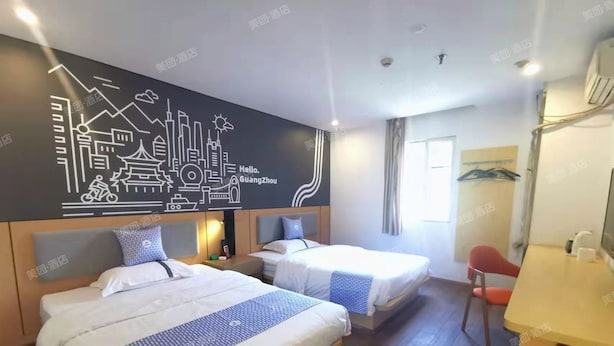 Ein Hotelzimmer mit zwei Betten, einem Schreibtisch und einer Wand mit Stadtbild-Mural.