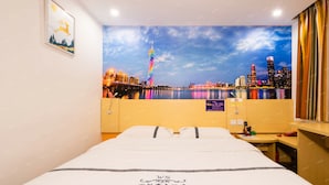Ein Hotelzimmer mit Bett, Nachttisch, Wandfernseher und Stadtbild-Mural.