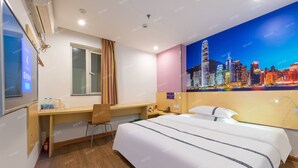 Ein Hotelzimmer mit Bett, Schreibtisch, Stuhl und Wandgemälde mit Stadtansicht.