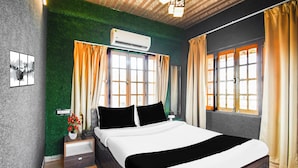 Habitación de hotel con cama, mesitas de noche, aire acondicionado instalado en la pared y una ventana con cortinas.