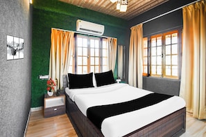 Habitación de hotel con cama, mesitas de noche, aire acondicionado instalado en la pared y una ventana con cortinas.