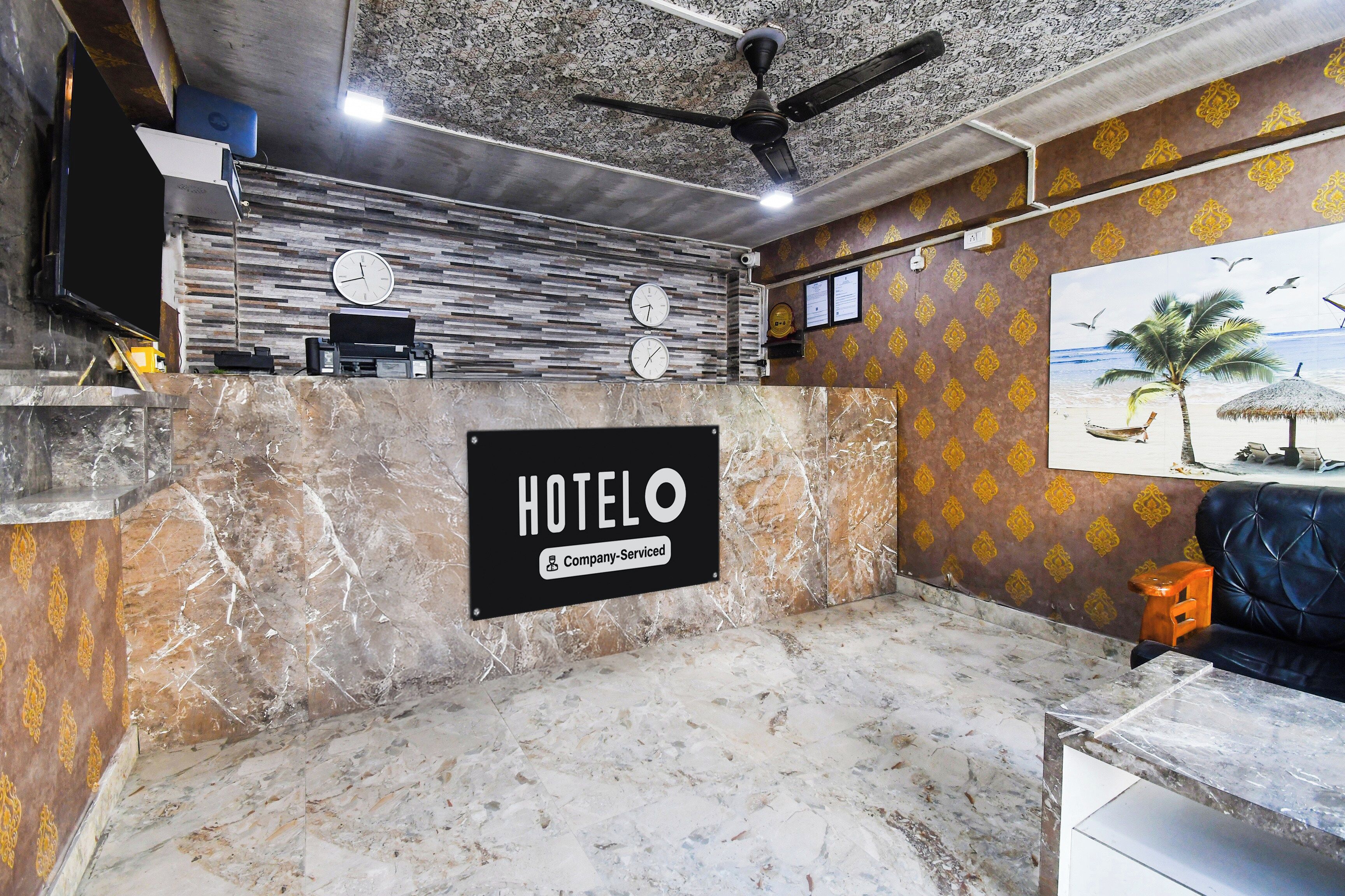 Zona de recepción de un hotel con mostrador de mármol, ventilador de techo y un reloj de pared.