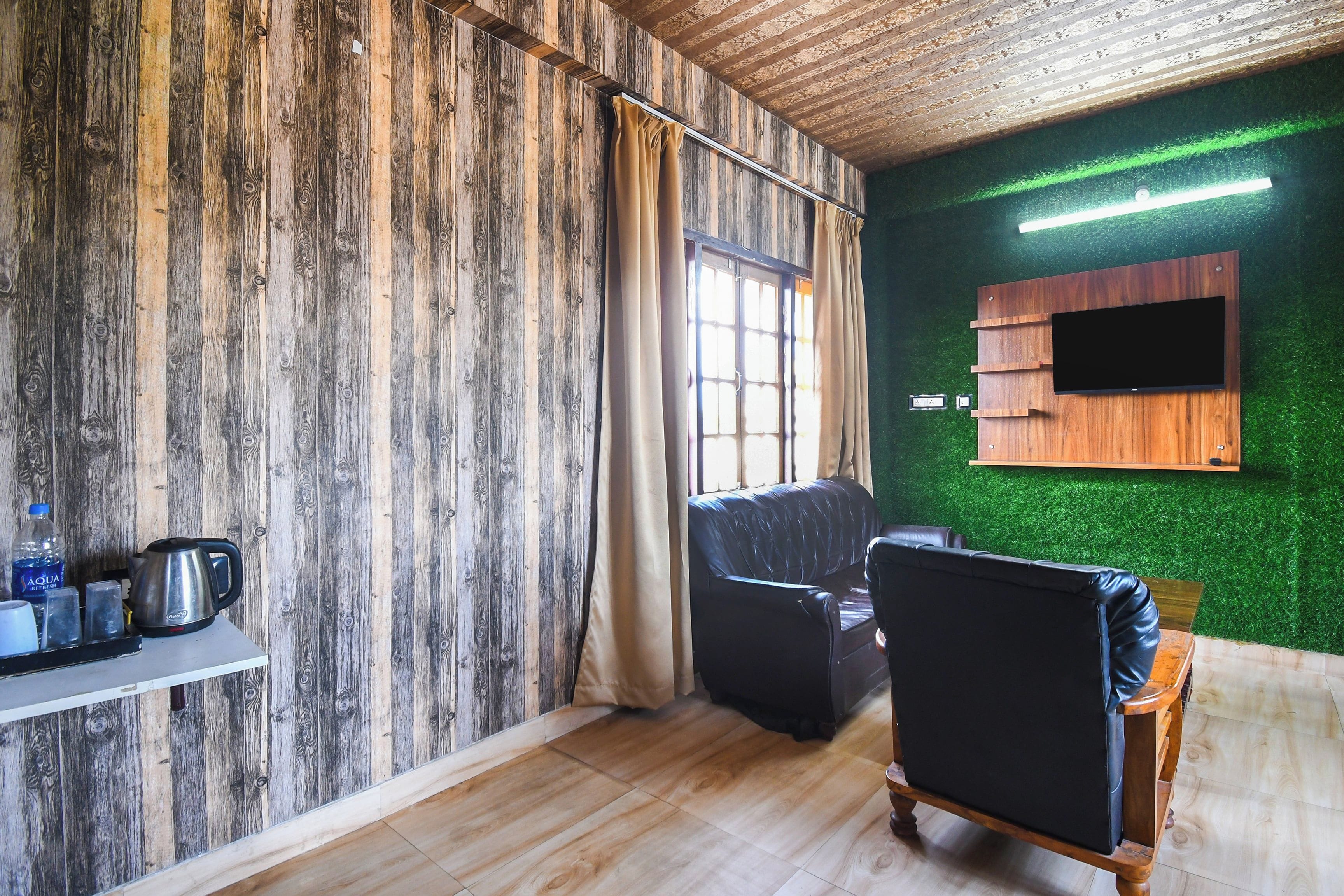 Una habitación con pared de madera, un sofá de cuero negro, un mueble de madera con televisor de pantalla plana y una pared con césped artificial verde.