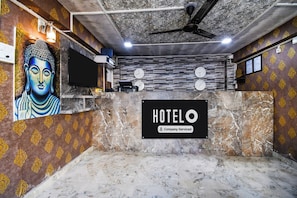 Zona de recepción de hotel con un mural de Buda, un reloj y un letrero que indica servicio de empresa.