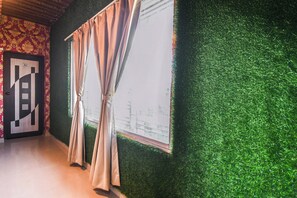 Una habitación con pared de césped artificial verde, una ventana con cortinas y una puerta con un letrero de número.