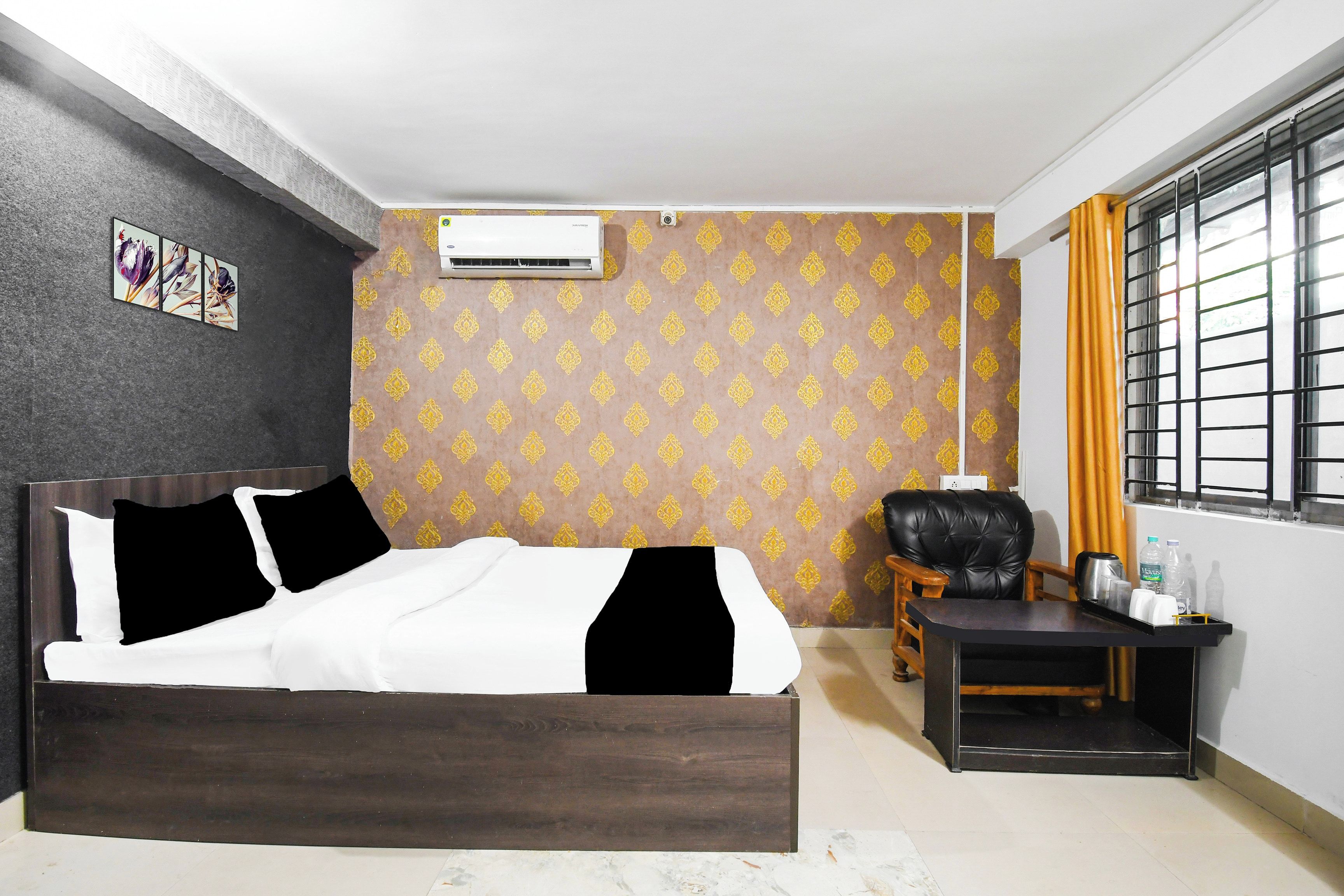 Un dormitorio con cama, una silla, una mesita, aire acondicionado y una ventana con cortinas.