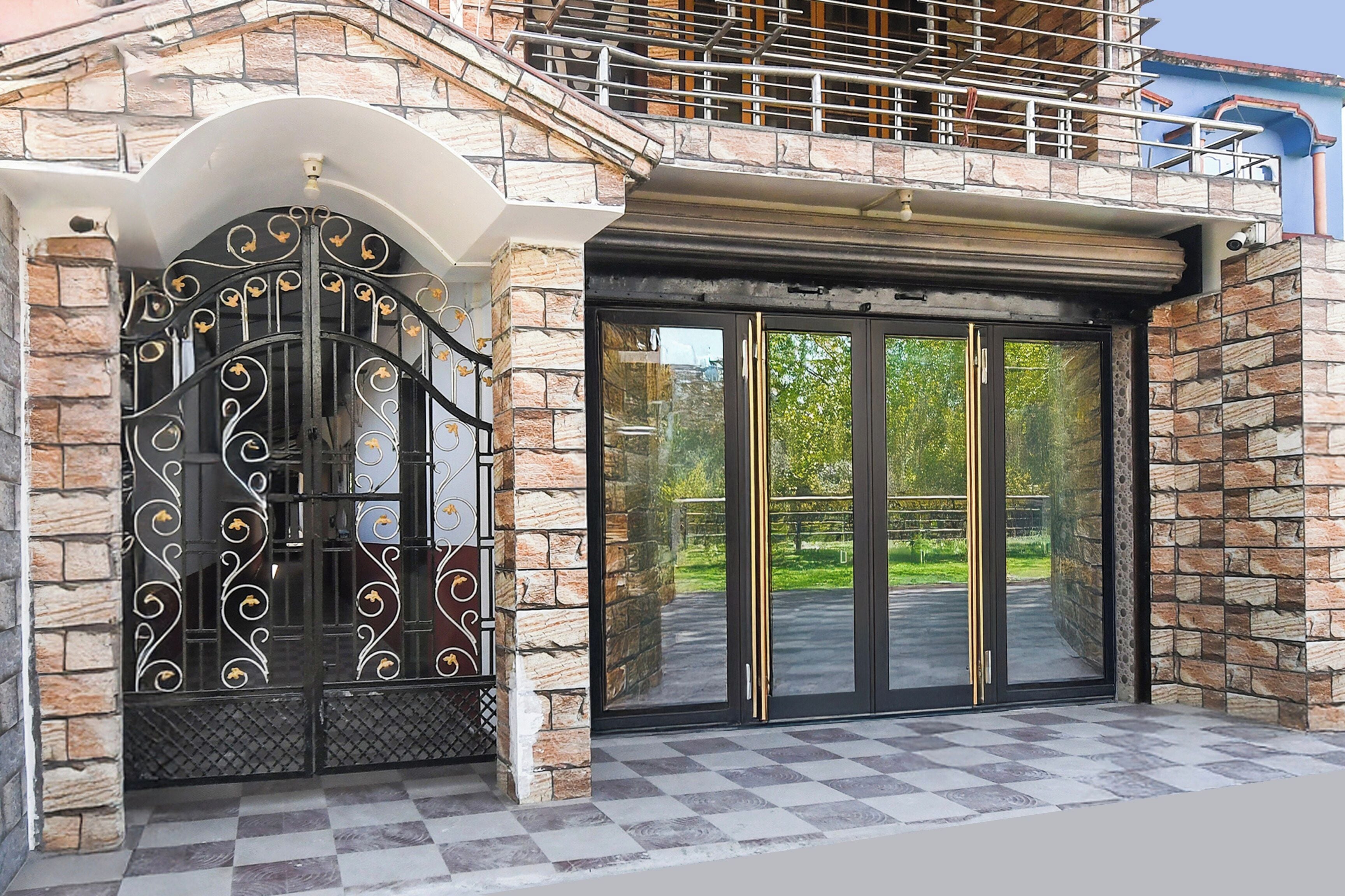 A building entrance with a decorative metal gate, a stone facade, and a glass door leading to a paved area.