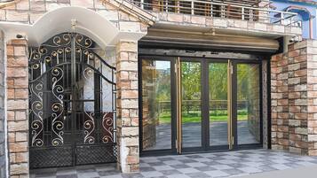 Una entrada de edificio con una puerta de metal decorativa, fachada de piedra y puerta de vidrio que da a una zona pavimentada.