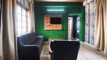 Una habitación con piso de madera, un sofá, una mesa y un televisor de pantalla plana montado en la pared.