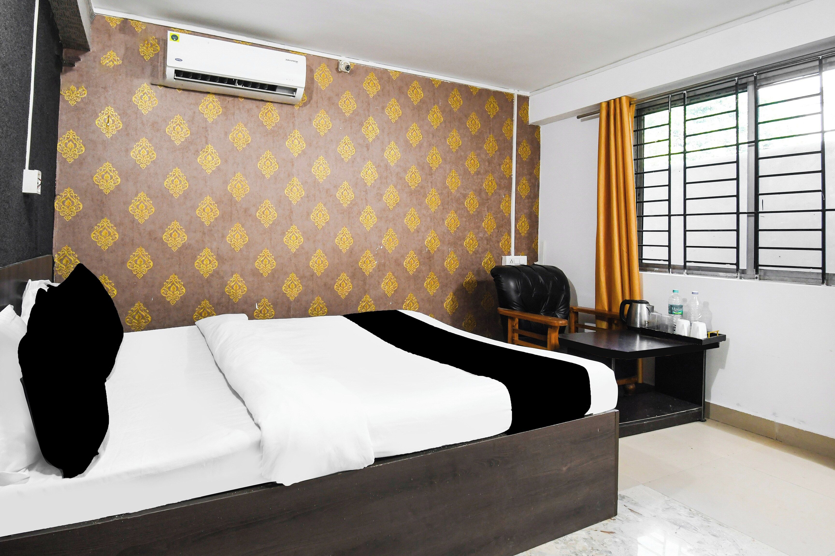 A hotel room with a bed, a desk, a chair, an air conditioning unit, and a window with curtains.
