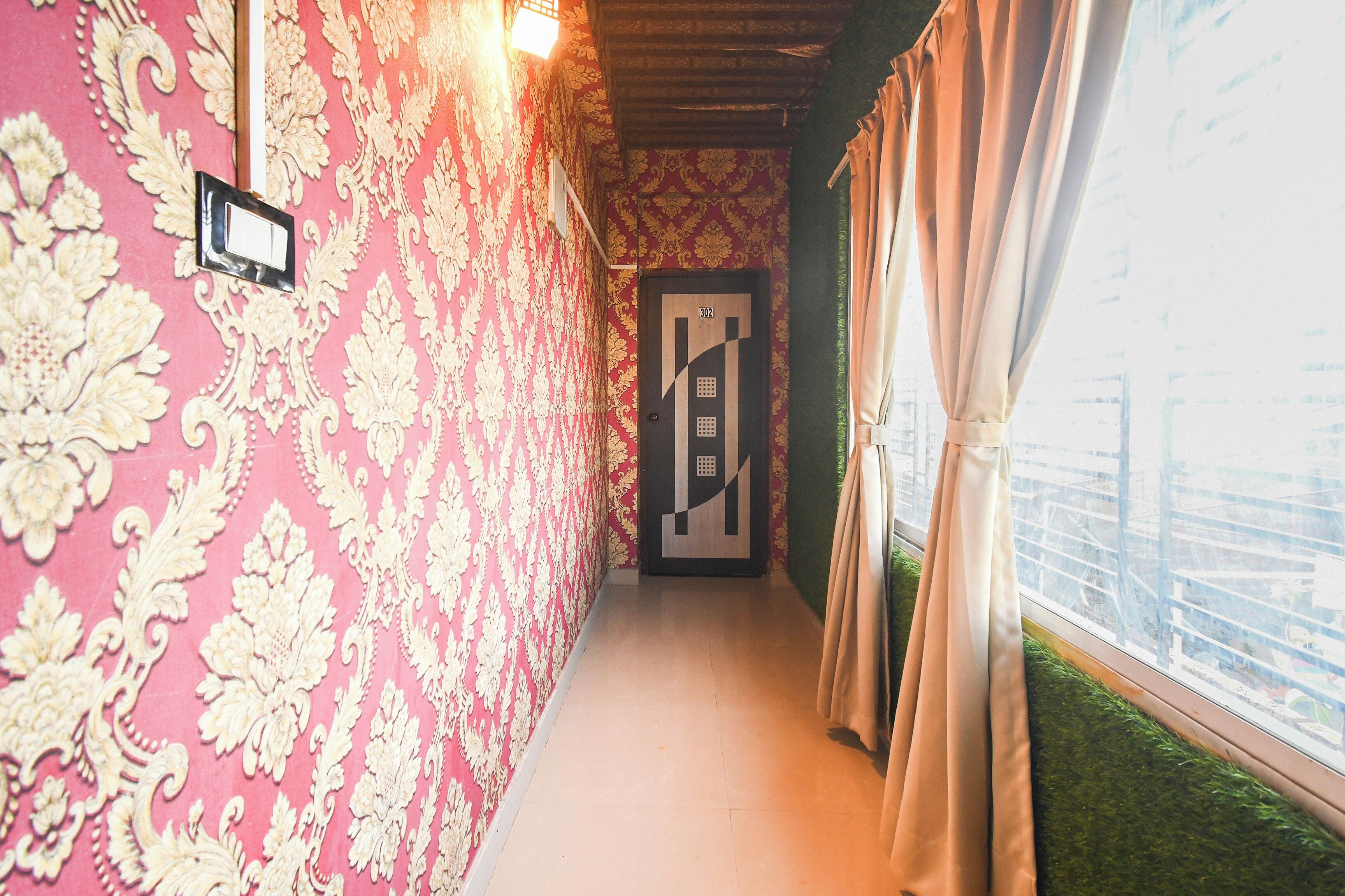A corridor with patterned wallpaper, a door with a number, and a window with curtains.