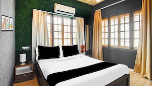 Habitación de hotel con cama, mesita de noche, lámpara, aire acondicionado montado en la pared y ventana con cortinas.