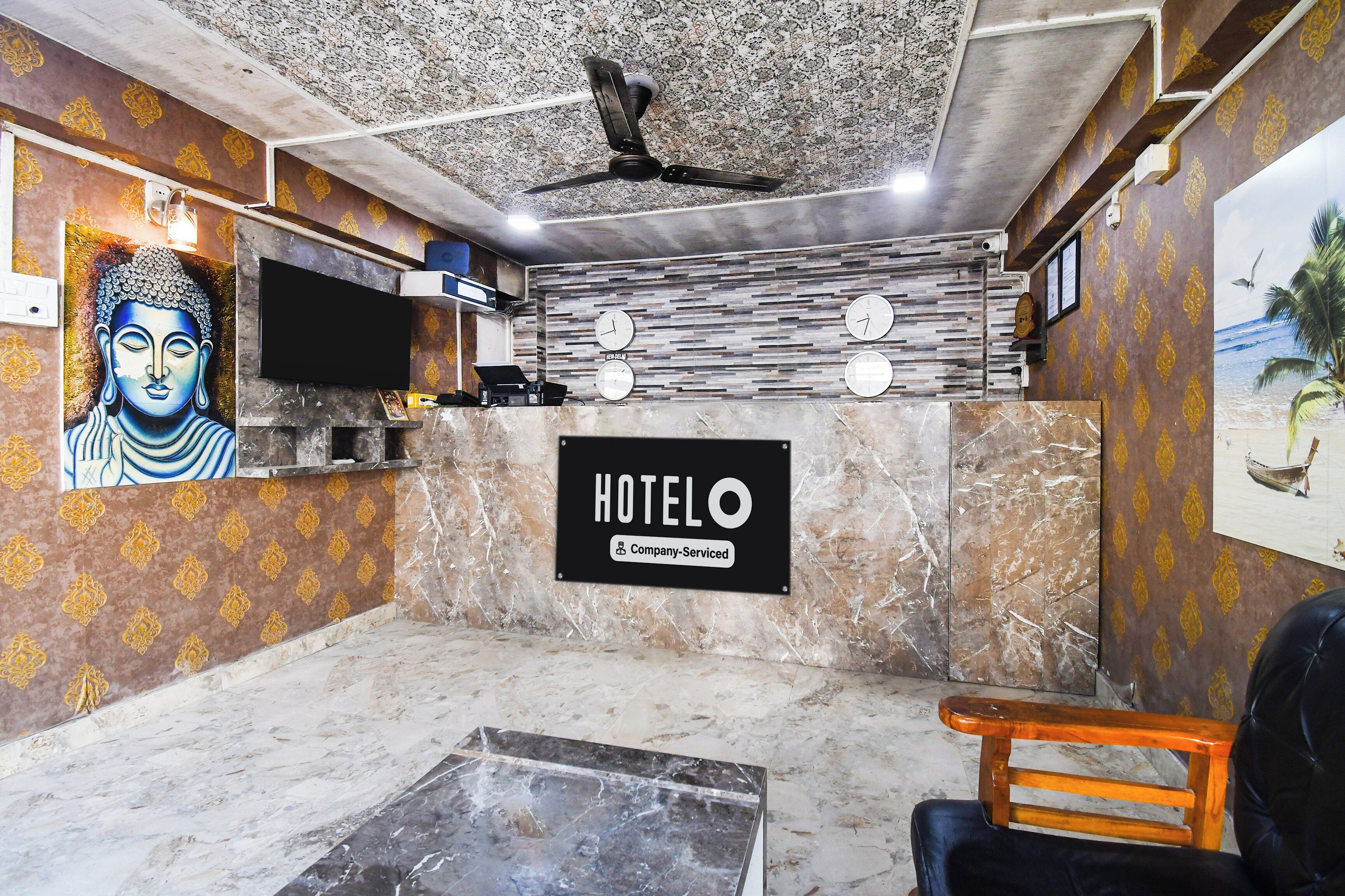 Zona de recepción de hotel con mostrador de mármol, estatua de Buda, ventilador de techo y un reloj de pared.