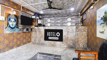 Zona de recepción de hotel con mostrador de mármol, estatua de Buda, ventilador de techo y un reloj de pared.