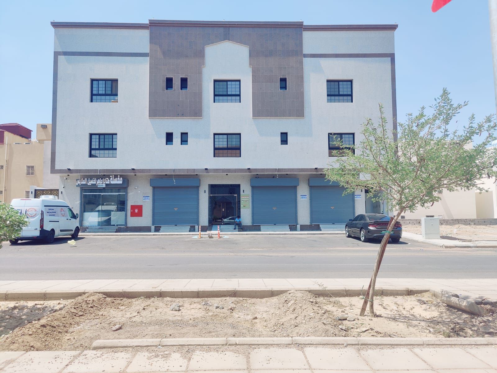 A multi-story building with a flat facade, several windows, and a ground-level entrance with a closed shutter.
