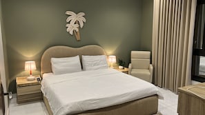 Une chambre d’hôtel comprenant un lit, deux tables de chevet avec des lampes, une chaise, une plante et un décor mural représentant un palmier.