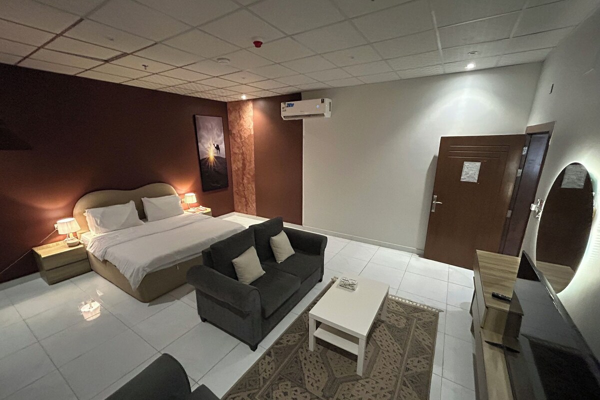 Une chambre d’hôtel avec un lit, un canapé, une table basse et une porte.