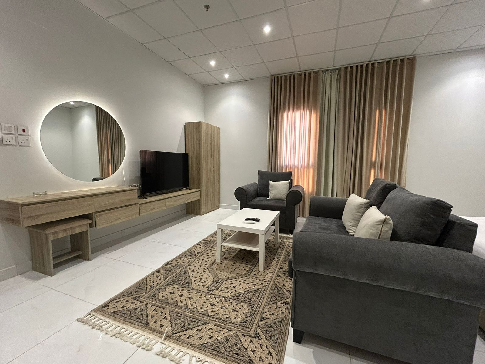 A modern living room with a flat-screen TV, a sofa, a coffee table, and a patterned rug.