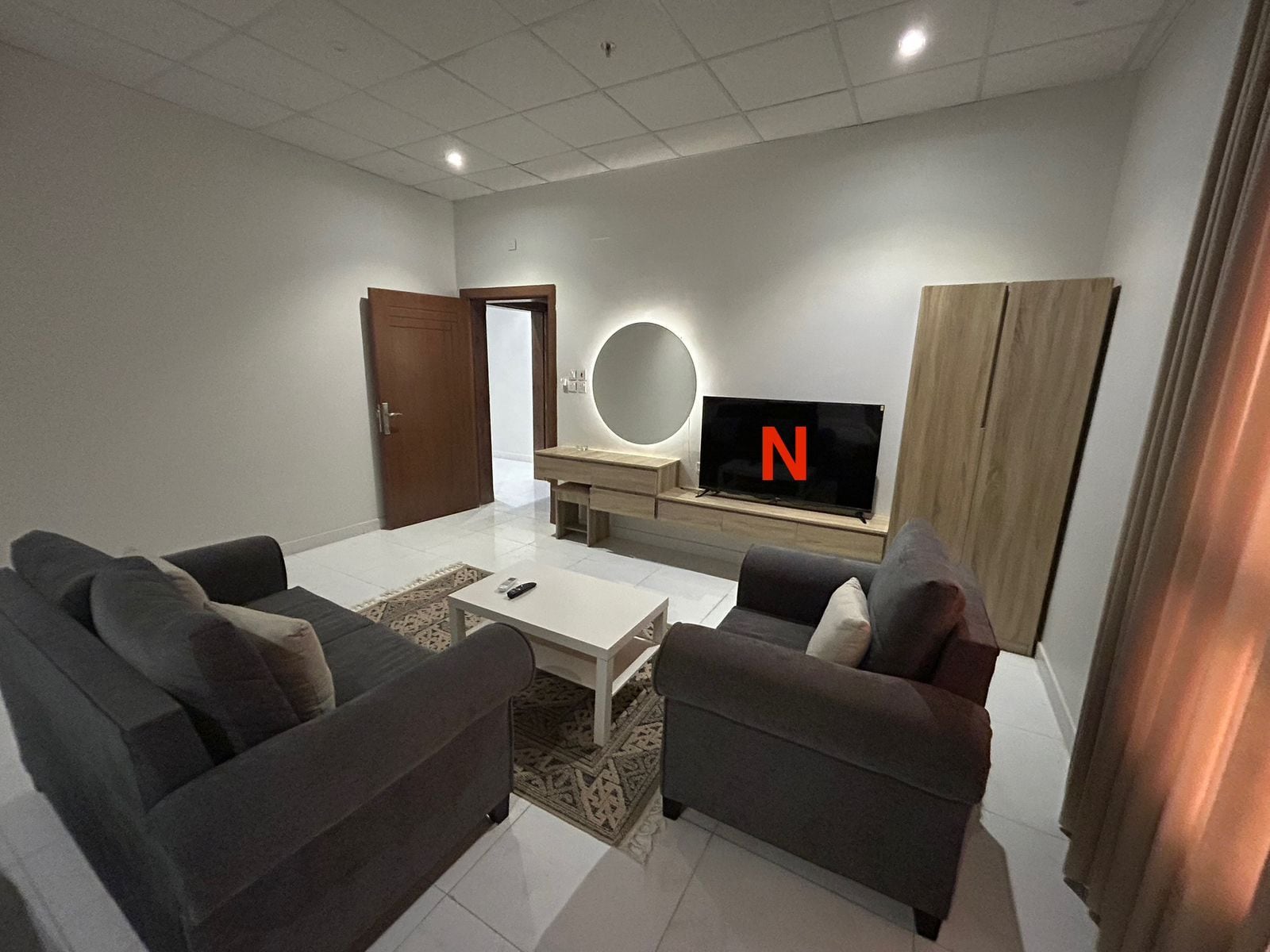 Una sala de estar moderna con un televisor de pantalla plana, dos sofás, una mesa de centro y un armario de madera.