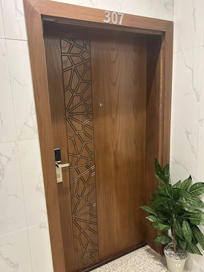 A wooden door with a geometric pattern, a number '307' above it, and a potted plant beside it. - Al Madinah Residential Apartments (Madinah)