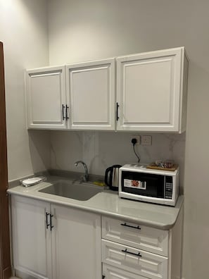 Une cuisine de taille réduite avec des meubles blancs, un évier, un four à micro-ondes et un grille-pain.
