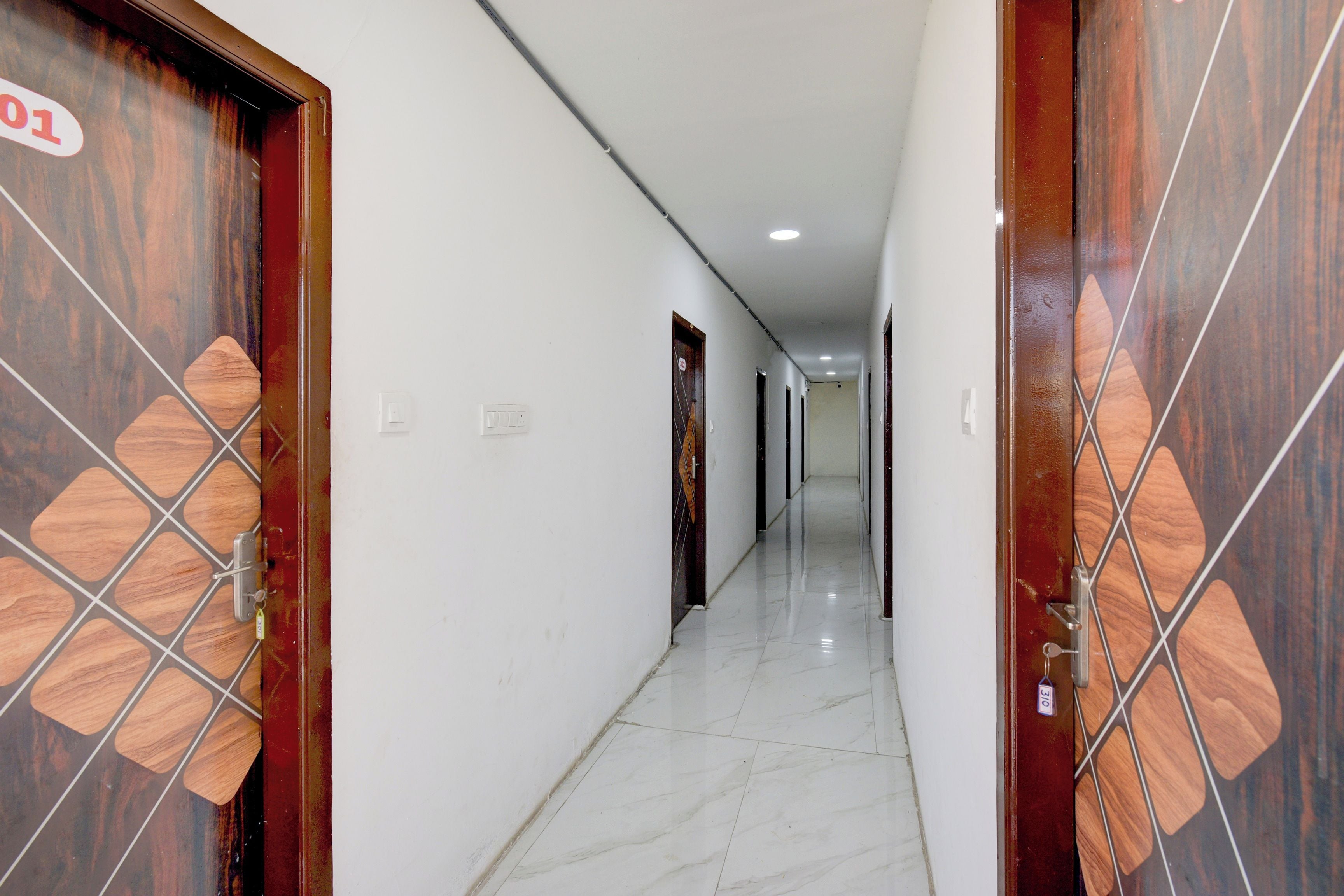 A corridor with doors on both sides, a tiled floor, and a light switch on the wall.