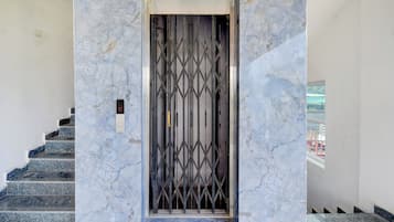 En hisskorg i marmor med en dörr av metallgaller, en trappa med marmortrappsteg och en väggmonterad kontrollpanel.
