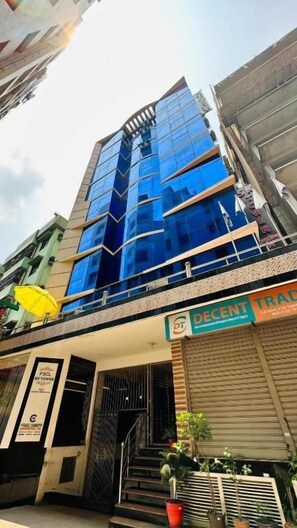 Un edificio de varios pisos con fachada de vidrio moderna, una entrada a nivel de calle con escaleras y un escaparate con señalización visible.