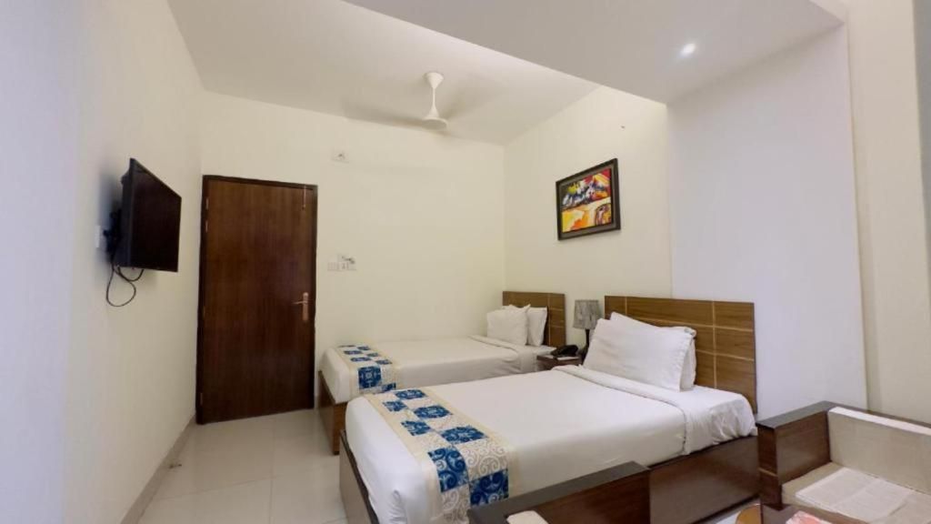 Habitación de hotel con dos camas, televisión, ventilador de techo y un cuadro en la pared.