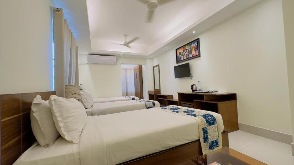 Quarto de hotel com duas camas, uma escrivaninha, televisão e ventilador de teto.