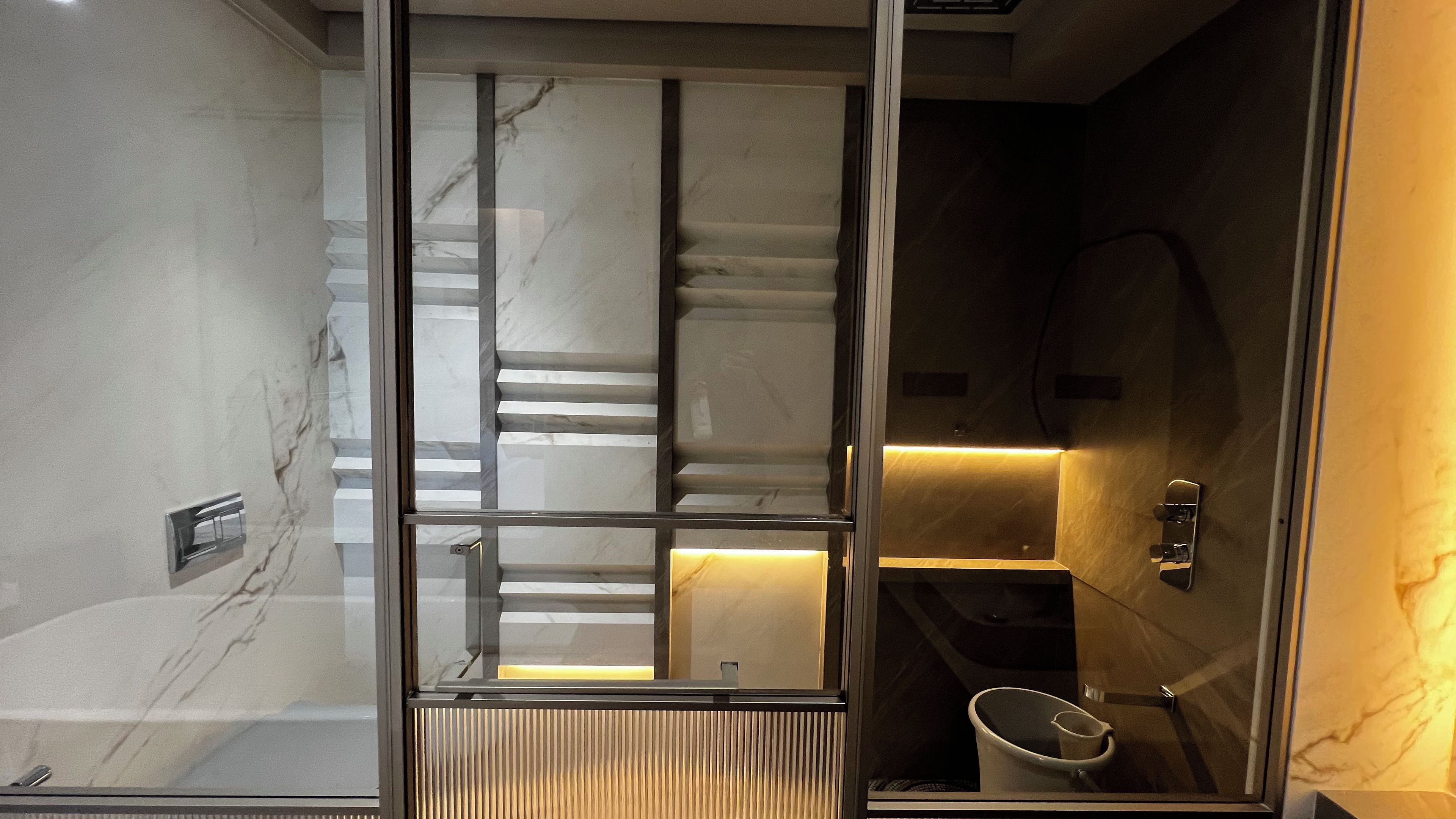 Un baño moderno con separador de vidrio, paredes de mármol y un inodoro empotrado.