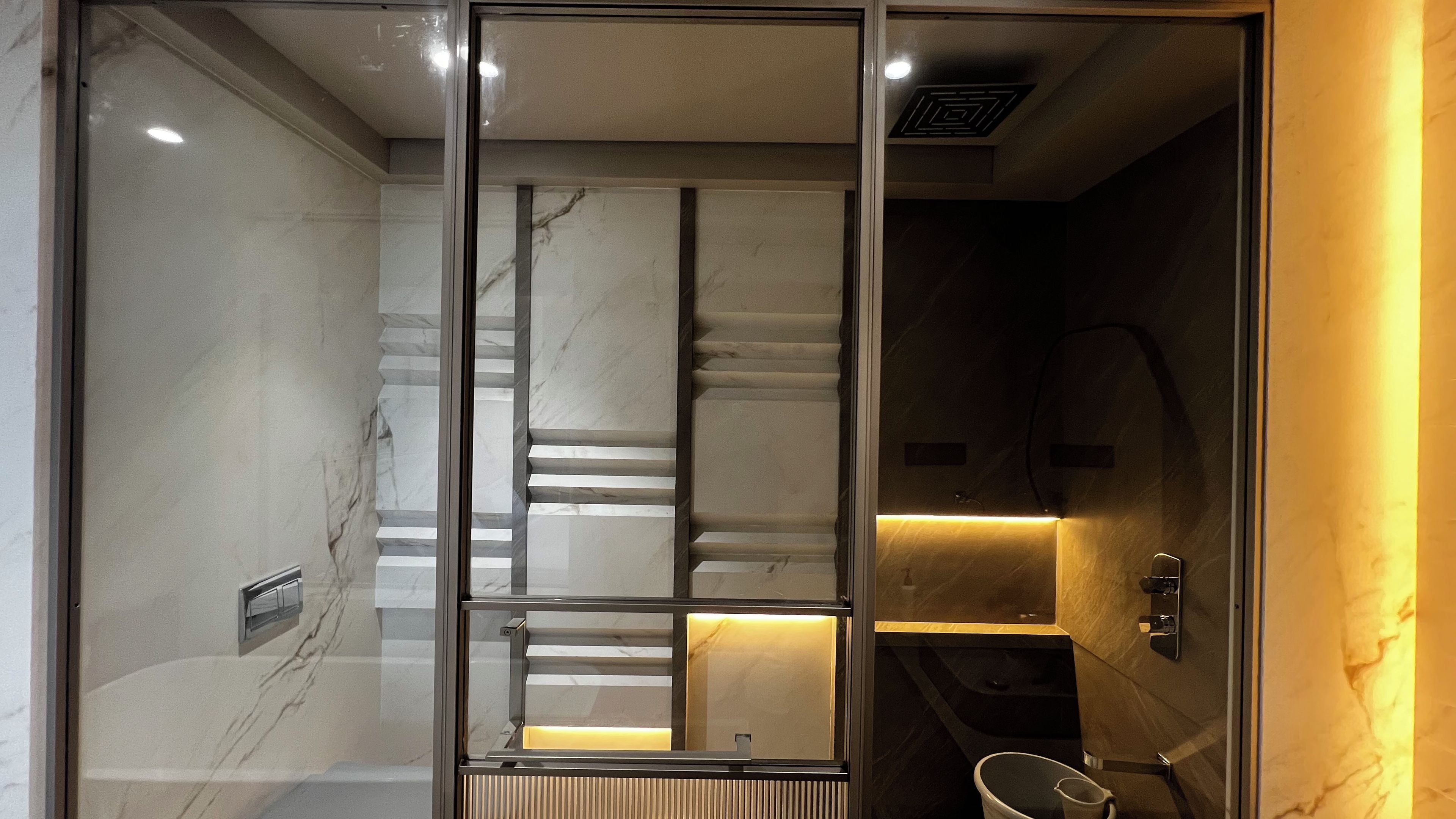 Un baño moderno con mampara de vidrio, paredes de mármol y lavamanos integrado.