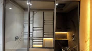 Un baño moderno con mampara de vidrio, paredes de mármol y lavamanos integrado.