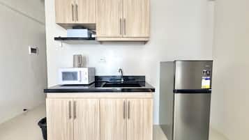 A compact kitchen with light wood cabinets, a stainless steel refrigerator, a microwave, and a black countertop.