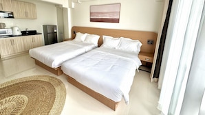 Quarto de hotel com duas camas, uma cozinha compacta e vista para a praia.