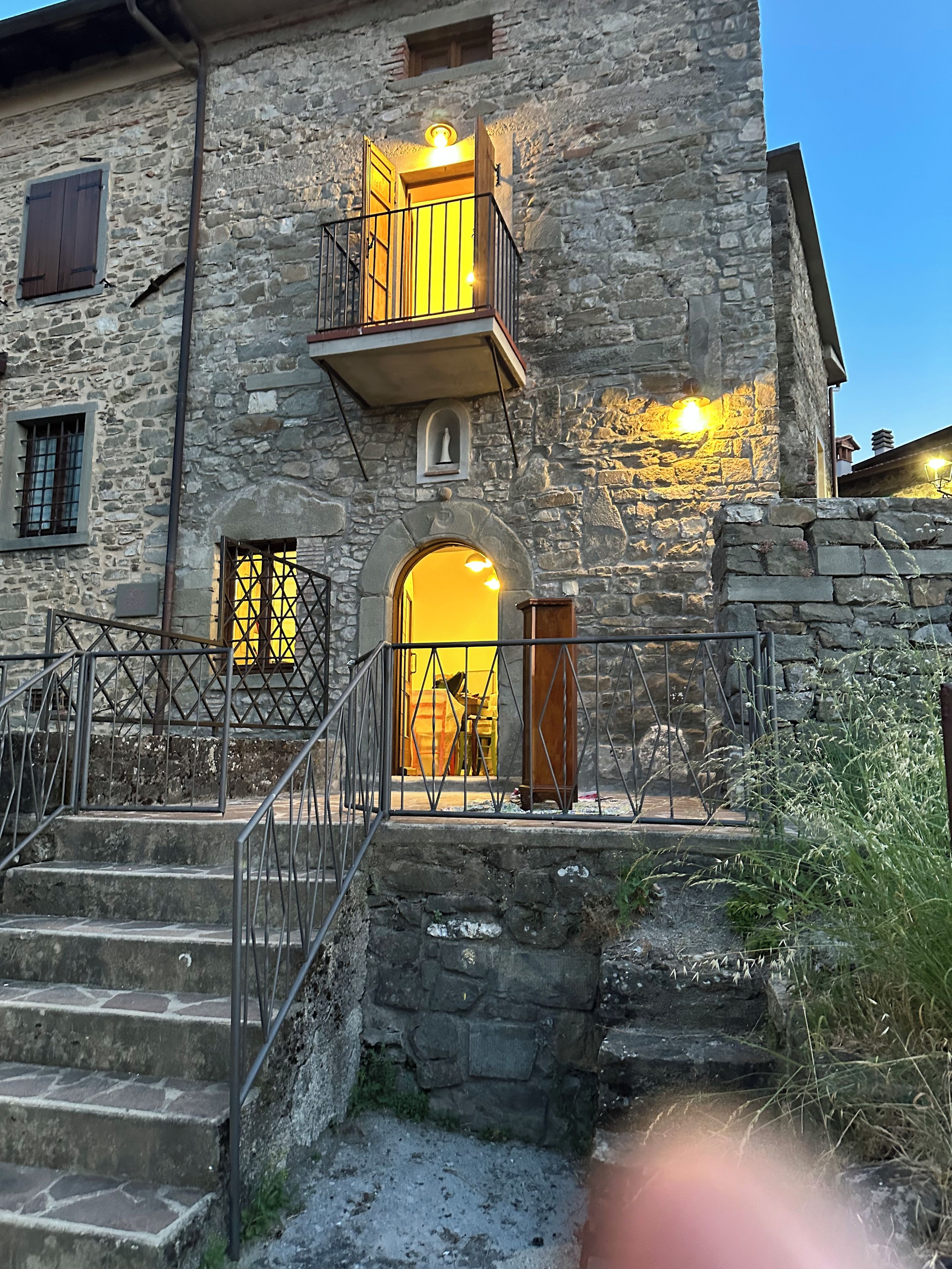 Un edificio in pietra con un balcone, una scala che conduce all'ingresso e una piccola statua sulla parete.