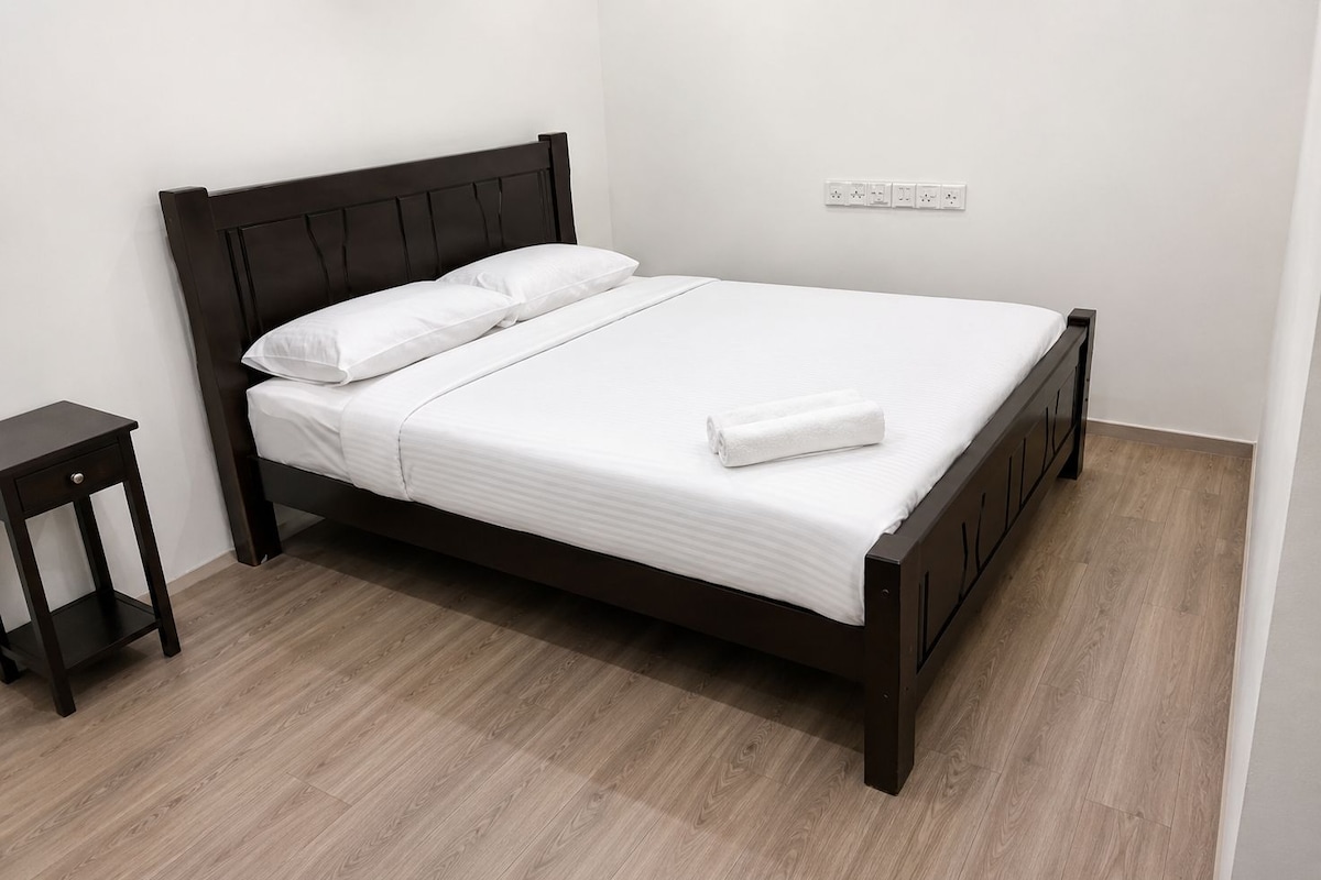 Una cama individual con cabecera oscura, ropa de cama blanca y una mesita de noche pequeña.