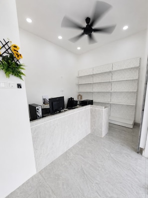 Un área de recepción con mostrador de mármol, ventilador de techo y estantería de pared.