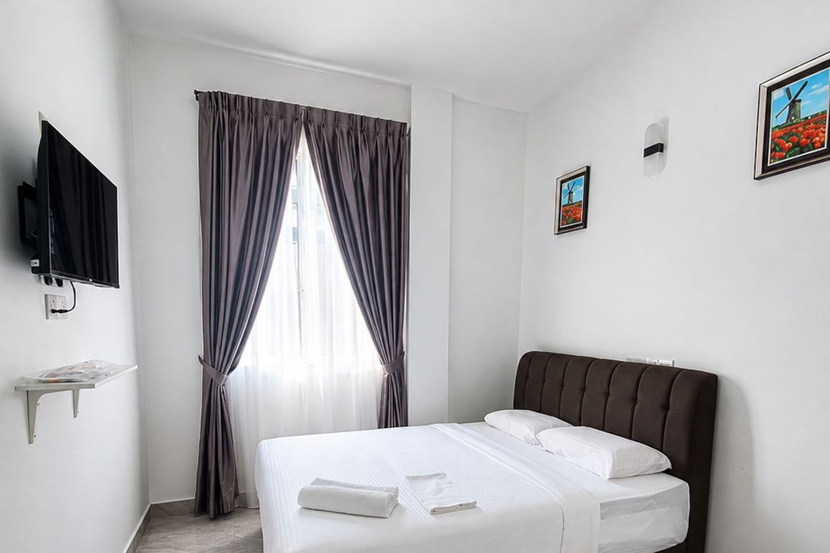 Una habitación de hotel moderna con una cama grande, un televisor de pantalla plana en la pared y una pequeña estantería.