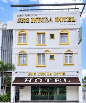 Un hotel de varios pisos con un cartel llamativo que dice 'SRG INDIRA HOTEL' y un toldo marrón debajo.