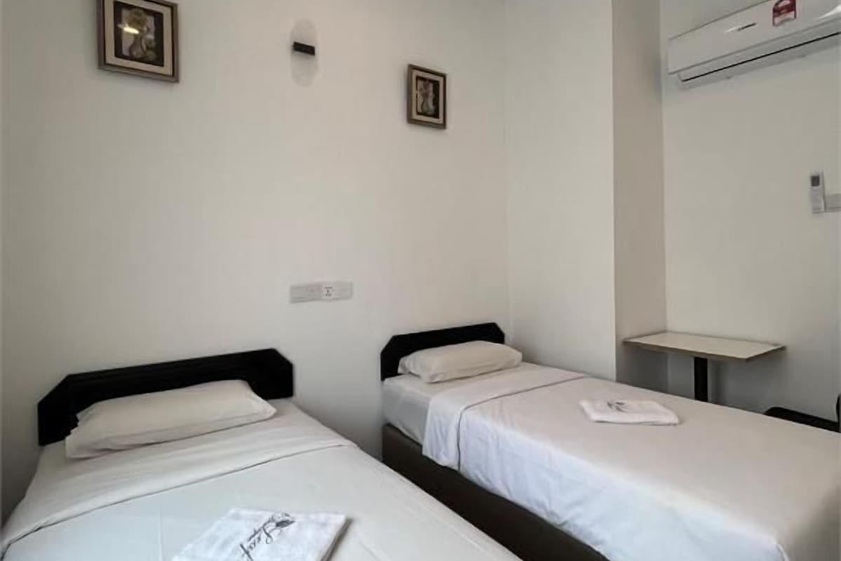 Habitación de hotel con dos camas individuales, una mesita pequeña y un equipo de aire acondicionado instalado en la pared.
