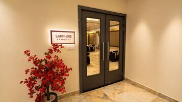 Entrada de hotel con un cartel que dice 'Sapphire Banquet', una puerta oscura y una planta en maceta con flores rojas.