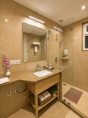 Un baño moderno con lavamanos de granito, cabina de ducha de cristal y un espejo grande.