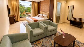 Una habitación de hotel con una cama, dos sofás, una mesita de centro y un ventanal con cortinas.