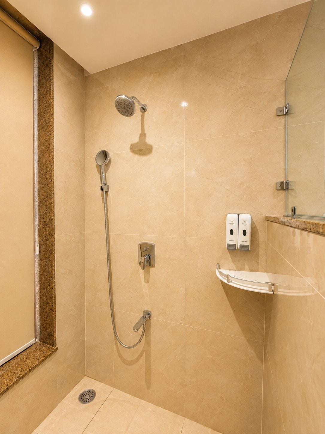 A modern bathroom with a walk-in shower, a handheld showerhead, a wall-mounted faucet, and a soap dispenser.